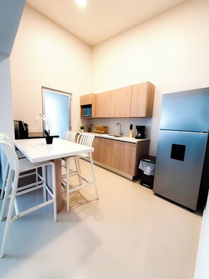 A modern kitchen with white cabinetry, a stainless steel refrigerator, and a dining area with white chairs and a table. - Brand New: Boutique House, Near LIR Airport & Best Beaches (Guanacaste Province)