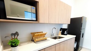 Een moderne keuken met houten kastjes, een RVS-spoelbak, een ingebouwde magnetron en een zwarte koelkast.