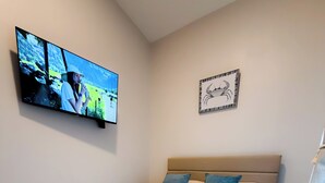 Een slaapkamer met een bed, een aan de muur bevestigde televisie en een lijst met een foto boven het bed.