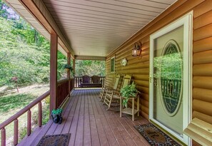 A wooden porch with a covered roof, a glass door with a decorative frame, and a view of a green landscape. - Bluebird`s Song 5BR, 3.5BA by HoneyBearCabins (Sevierville)