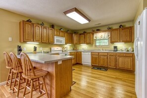 A kitchen with wooden cabinets, a central island with bar stools, a microwave, and a dishwasher. - Bluebird`s Song 5BR, 3.5BA by HoneyBearCabins (Sevierville)