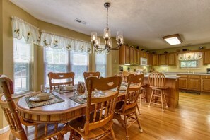 A dining area with a wooden table and chairs, a chandelier, and a kitchen in the background. - Bluebird`s Song 5BR, 3.5BA by HoneyBearCabins (Sevierville)
