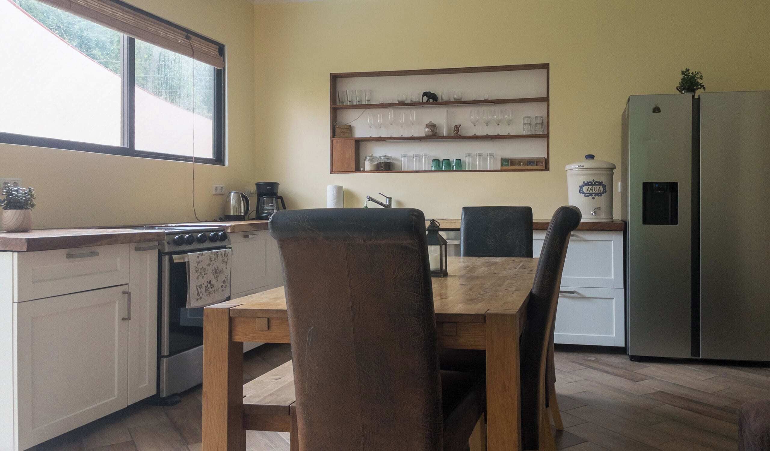Eine Küche mit Esstisch, Stühlen, einem Kühlschrank und einem Fenster.