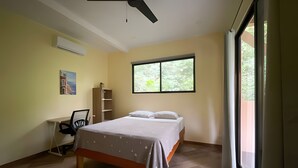 Une chambre à coucher comprenant un lit, un bureau, une chaise, un ventilateur de plafond et une fenêtre donnant sur un paysage verdoyant.