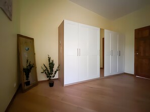 Una habitación con piso de madera, un armario blanco, una planta en maceta y una puerta.