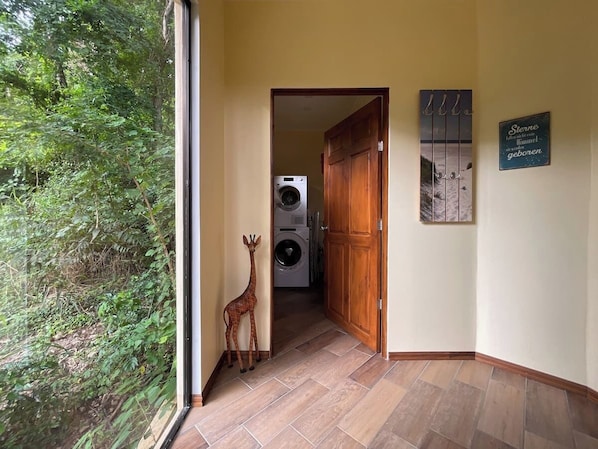 A hallway with a wooden door leading to a laundry room, a giraffe decoration, and a wall with a German phrase.