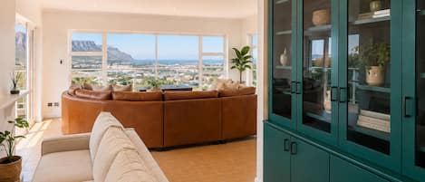 Una sala de estar con sofá, un aparador y vistas de la ciudad a través de amplios ventanales.