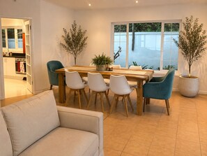 A dining area with a wooden table and white chairs, potted plants, and a view through large windows. - Sky Nova Villa False Bay Mountain & Ocean Views (Cape Town)