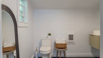 Ein Badezimmer mit Toilette, Bidet, Spiegel, Fenster und einer kleinen Pflanze.