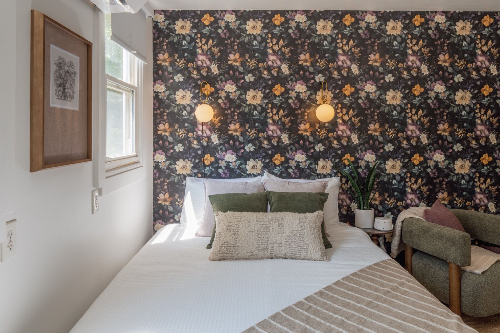 Une chambre à coucher avec un papier peint à motifs floraux, un lit avec des oreillers, une table de chevet avec une lampe et une chaise.