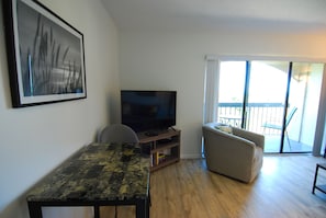 Ein Wohnzimmer mit einem Flachbildfernseher auf einem Holzboden, einer Couch, einem kleinen Tisch und einem Balkon mit Blick.