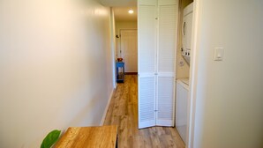 Um corredor estreito com piso de madeira, uma porta fechada e uma área de lavanderia visível, com uma máquina de lavar.