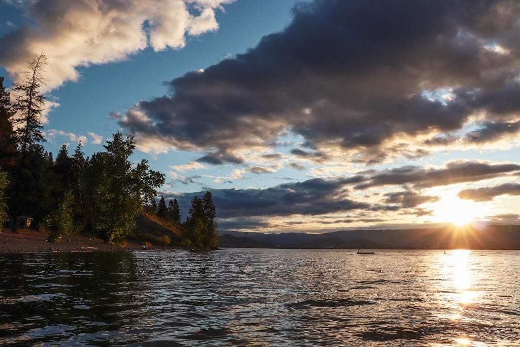 A body of water with a sunset, trees, and a distant shoreline.