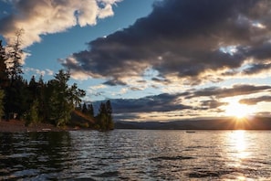 Un plan d’eau avec un coucher de soleil, des arbres et une côte lointaine.