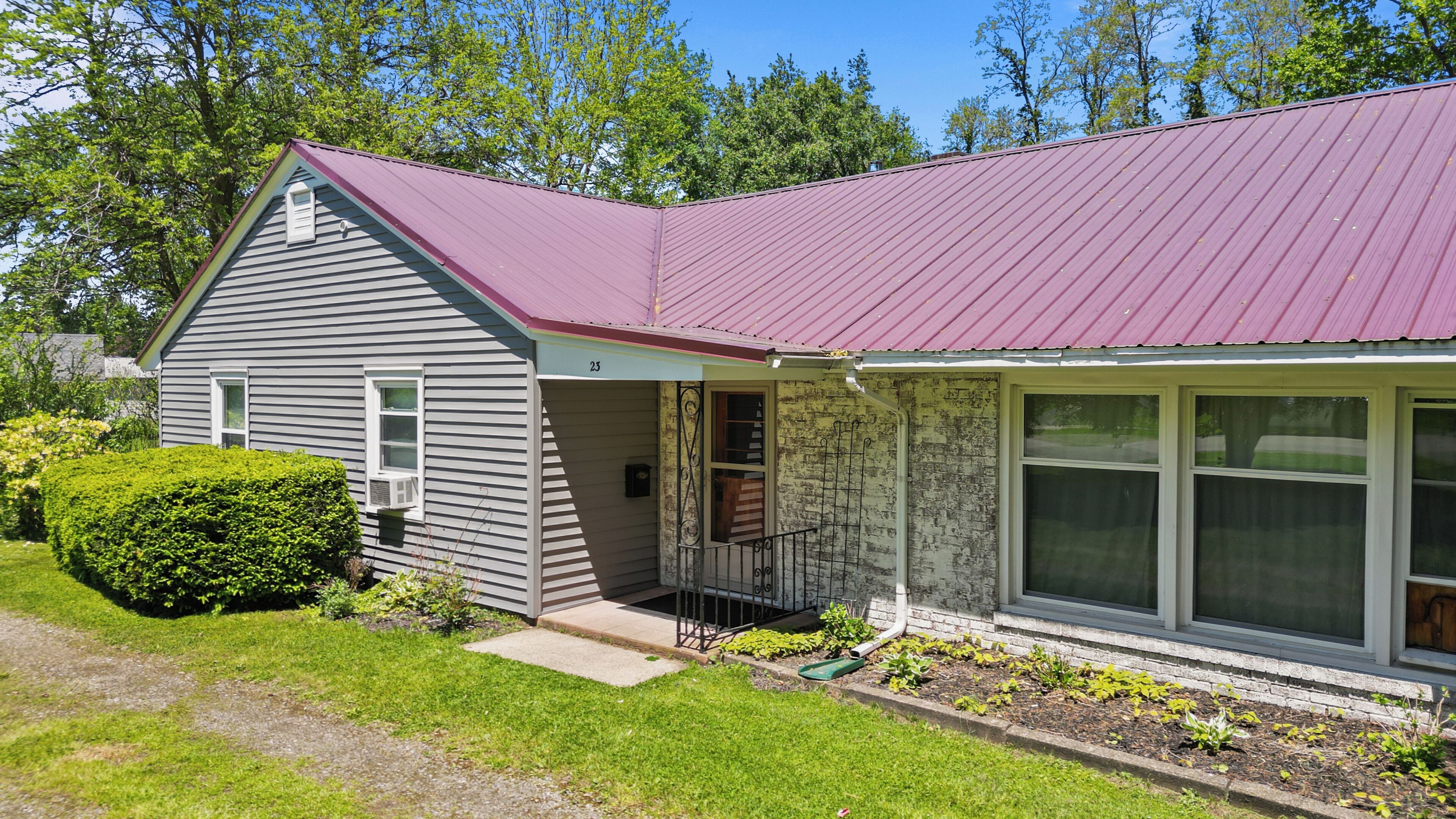 A single-story house with a red metal roof, a front porch, and a large window.