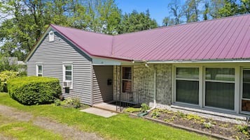 A single-story house with a red metal roof, a front porch, and a large window.