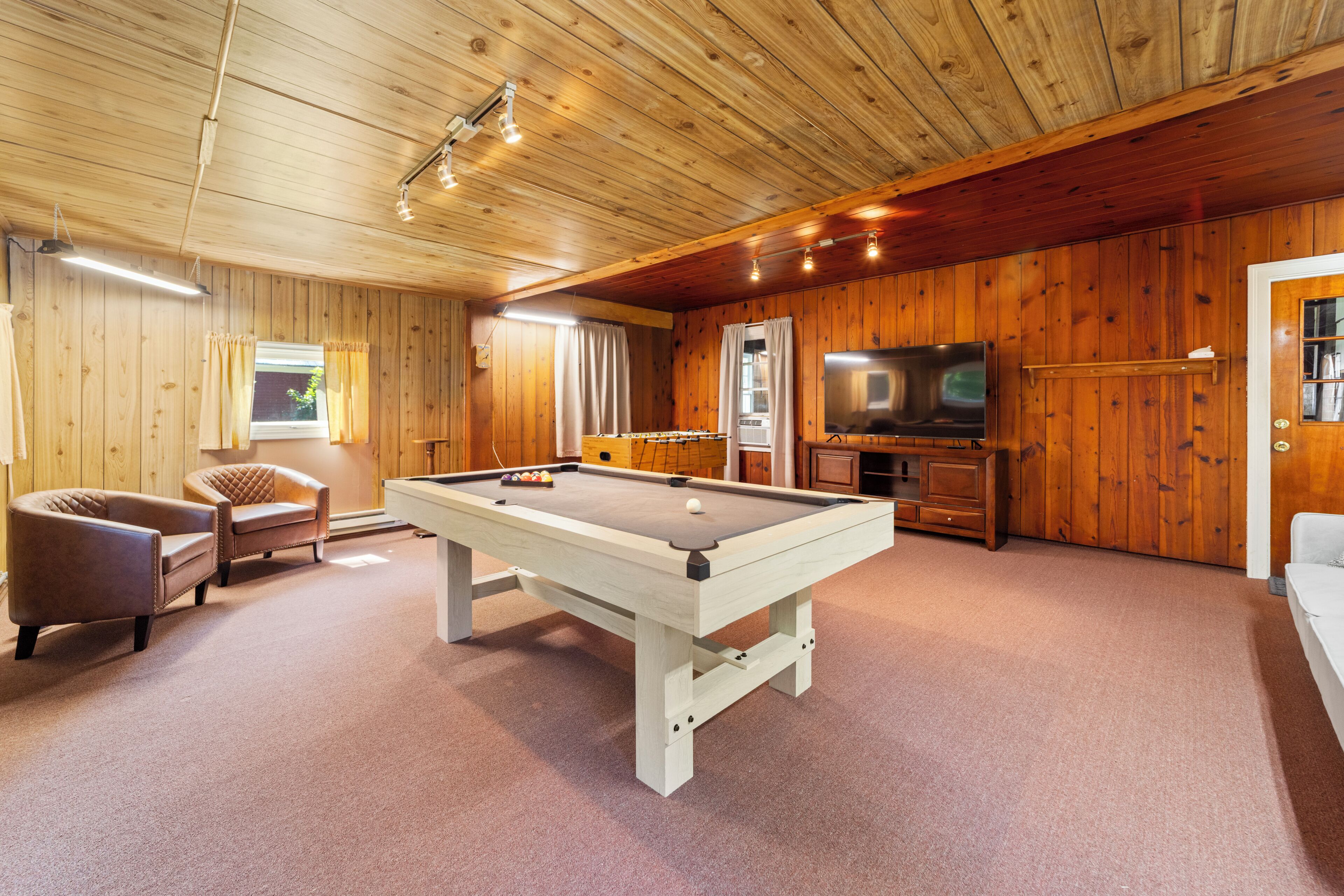 A pool table in a room with wooden walls and a television.