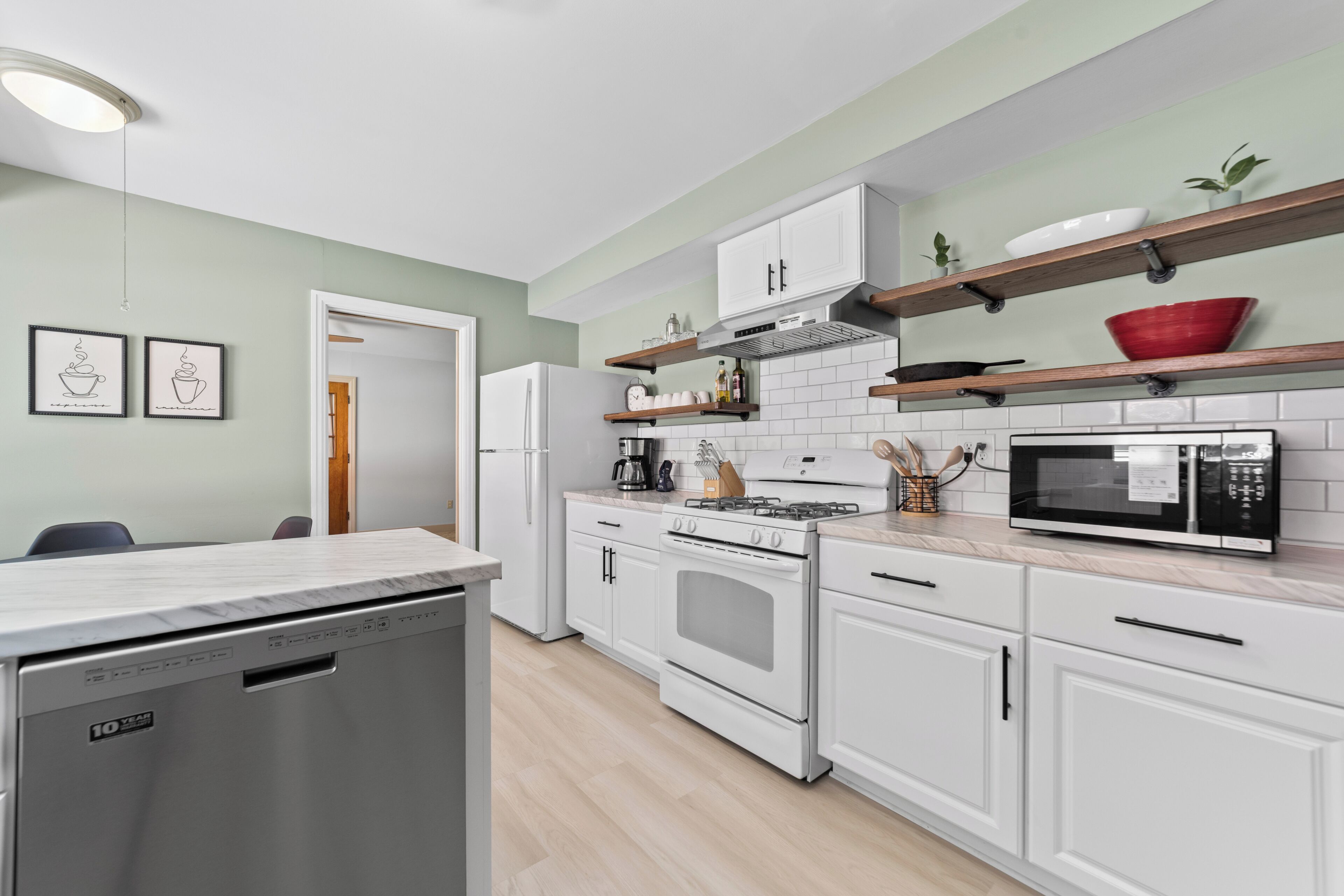 A modern kitchen with white cabinetry, a built-in oven, a microwave, and a coffee machine.