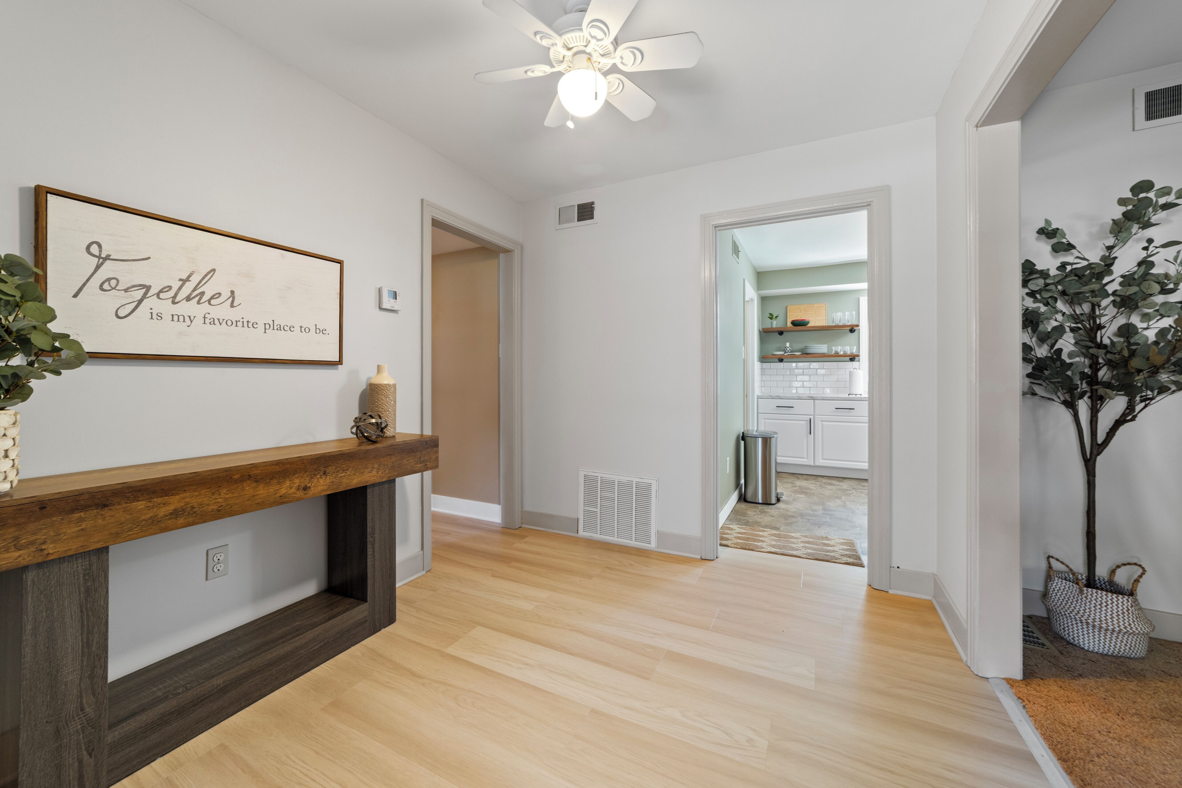 A hallway with a wooden bench, a ceiling fan, and a kitchen visible through an open door.
