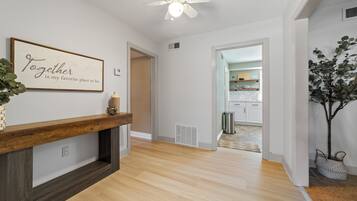 A hallway with a wooden bench, a ceiling fan, and a kitchen visible through an open door.