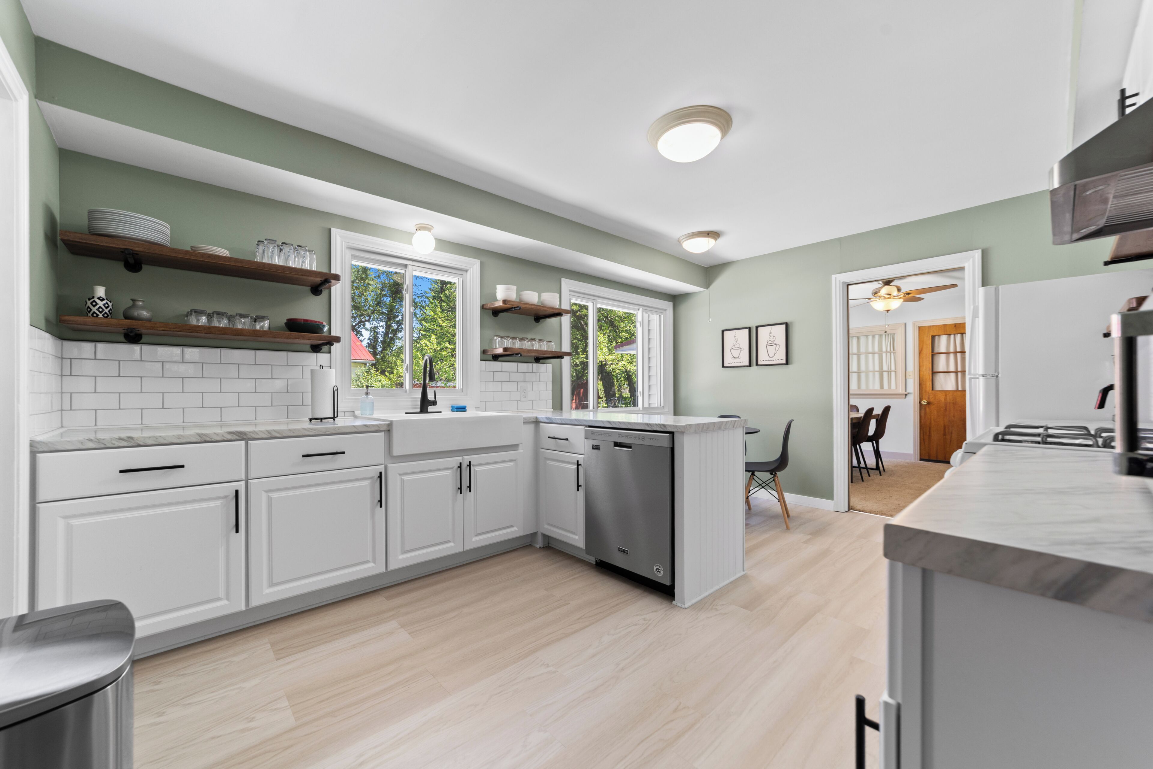 A modern kitchen with white cabinetry, a dishwasher, and wooden shelves.