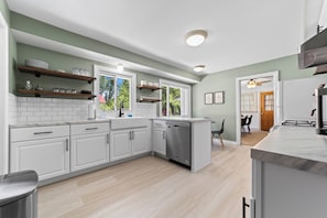 A modern kitchen with white cabinetry, a dishwasher, and wooden shelves. - Spacious 3BR Home with Pool Table & Patio Near Lake Erie (Westfield)