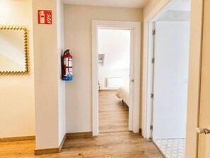 A hallway with a fire extinguisher mounted on the wall, leading to a bedroom with a bed and a radiator. - Casa Corbán by Wehomes (128) (Santander)