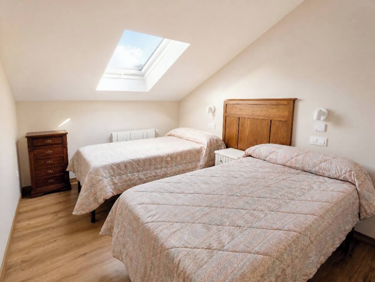 Een slaapkamer met twee bedden, een houten dressoir, een dakraam en een radiator.