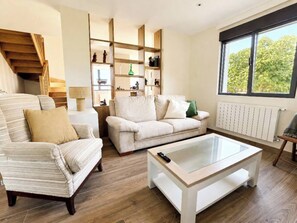 A living room with a sofa, armchair, and coffee table, wooden flooring, and a window with a view. - Casa Corbán by Wehomes (128) (Santander)