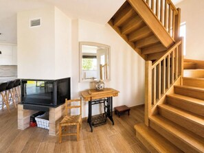 A modern living room with a wooden staircase, a television, a sewing machine, and a dining area with chairs. - Casa Corbán by Wehomes (128) (Santander)