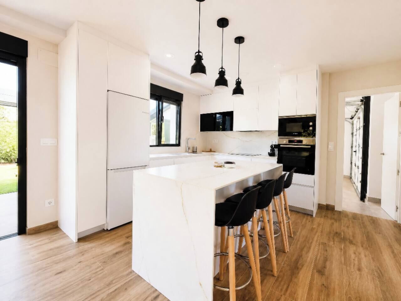 Een moderne keuken met een centraal eiland, zwarte barstoelen en hanglampen.