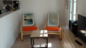 A small, bright room with two wooden chairs, a small table, a coffee machine, a TV, and a window. - Our house, just 4 minutes from the beaches (La Guérinière)