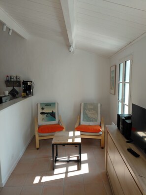 A small, bright room with two wooden chairs, a small table, a coffee machine, a TV, and a window. - Our house, just 4 minutes from the beaches (La Guérinière)