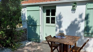 A patio with a table and chairs, a green door, and a white wall. - Our house, just 4 minutes from the beaches (La Guérinière)