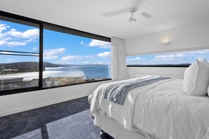 Quarto de hotel com uma grande janela que oferece vista para o mar e colinas distantes.