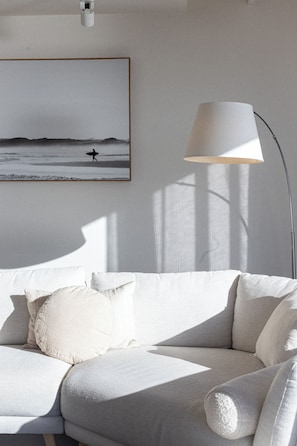 A modern living room with a grey sofa, a framed picture of a beach scene, and a floor lamp. - Suncoast Summer House Stunning River Derwent Vista (Blackmans Bay)