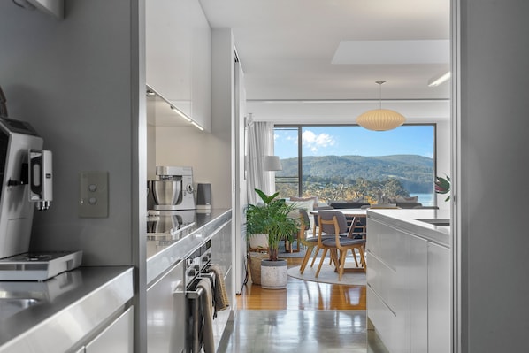 Cozinha moderna com eletrodomésticos de aço inoxidável, área de refeições com vista para as montanhas e uma grande janela.