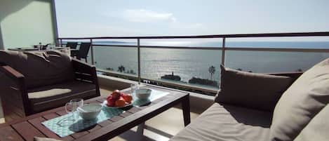 A balcony with a view of the sea, furnished with a sofa, a table, and a chair.