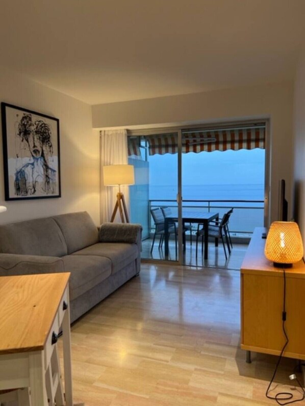 A room with a sofa, a table, a lamp, and a view of the sea through a sliding door.