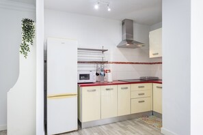 Eine kompakte Küche mit einem weißen Kühlschrank, einer Mikrowelle und einem Herd auf einer roten Arbeitsplatte. Es gibt beigefarbene Schränke mit silbernen Griffen sowie eine rote und weiße Spritzschutzwand.