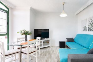 Ein Wohnzimmer mit Fernseher, einer Couch und einem Essbereich mit Stühlen und Tisch.