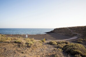A coastal landscape with a rocky beach, a clear sky, and a hilly terrain.