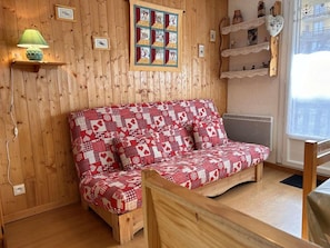 A cozy room with a wooden wall, a patterned sofa, a lamp, and a quilt. - 50m from ski slopes, Ground floor, balcony, tv, ski locker, 26m², Risoul (Risoul)
