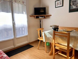 A room with a wooden dining table, chairs, a television on a shelf, and a window with curtains. - 50m from ski slopes, Ground floor, balcony, tv, ski locker, 26m², Risoul (Risoul)