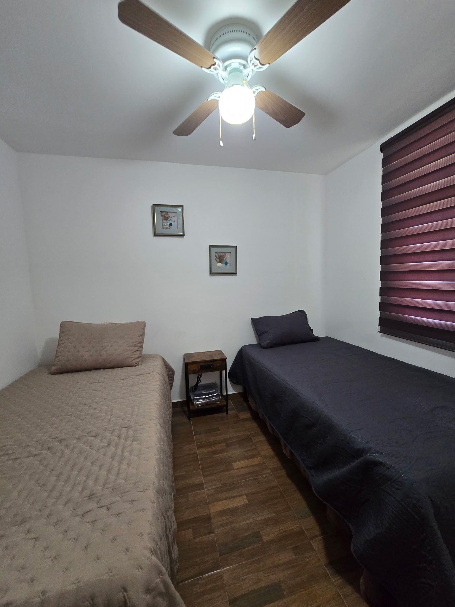 Un dormitorio con dos camas individuales, ventilador de techo y ventana con persianas.