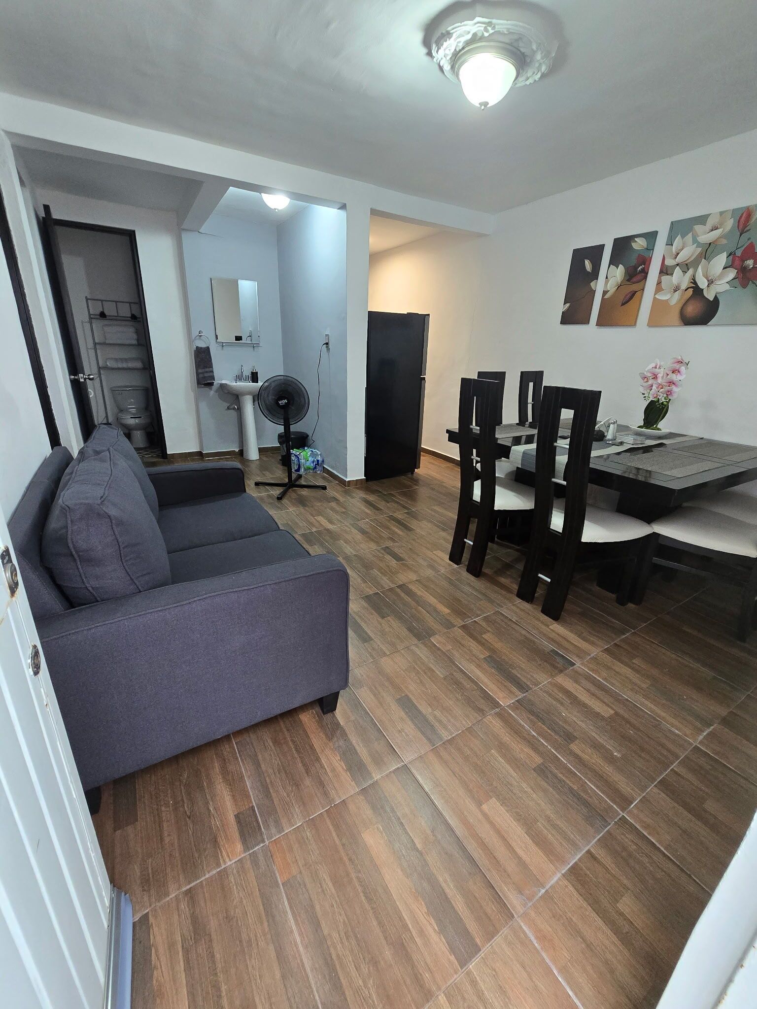 Ein modernes Wohnzimmer mit einem grauen Sofa, einem Essbereich mit Tisch und Stühlen und einer Küche im Hintergrund.