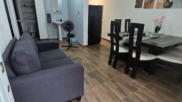 Ein modernes Wohnzimmer mit einem grauen Sofa, einem Essbereich mit Tisch und Stühlen und einer Küche im Hintergrund.