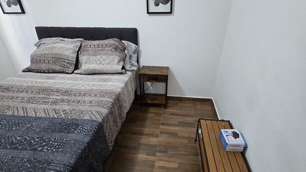 A bedroom with a bed, a nightstand, a wooden table, and a framed picture on the wall.