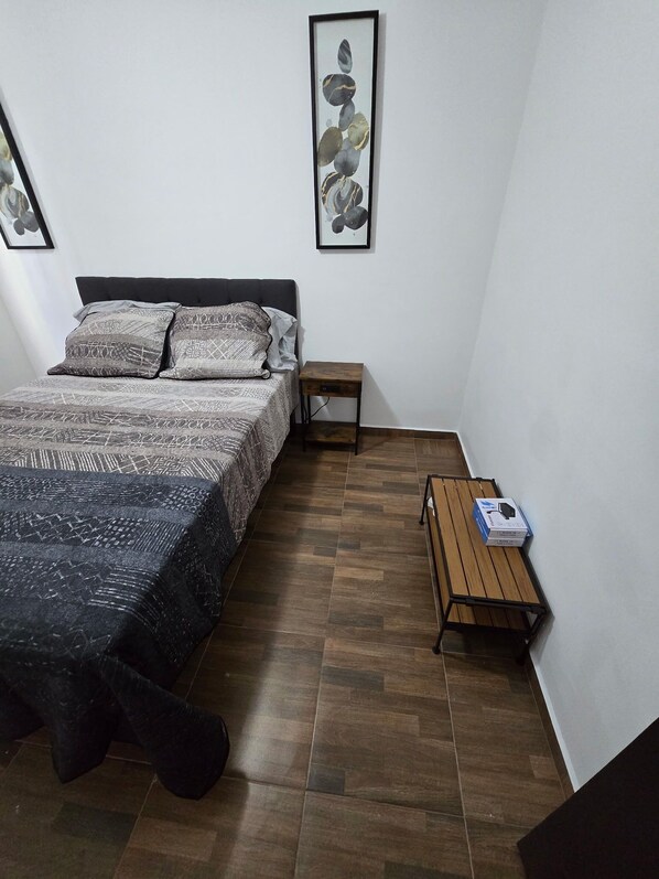 A bedroom with a bed, a nightstand, a wooden table, and a framed picture on the wall.