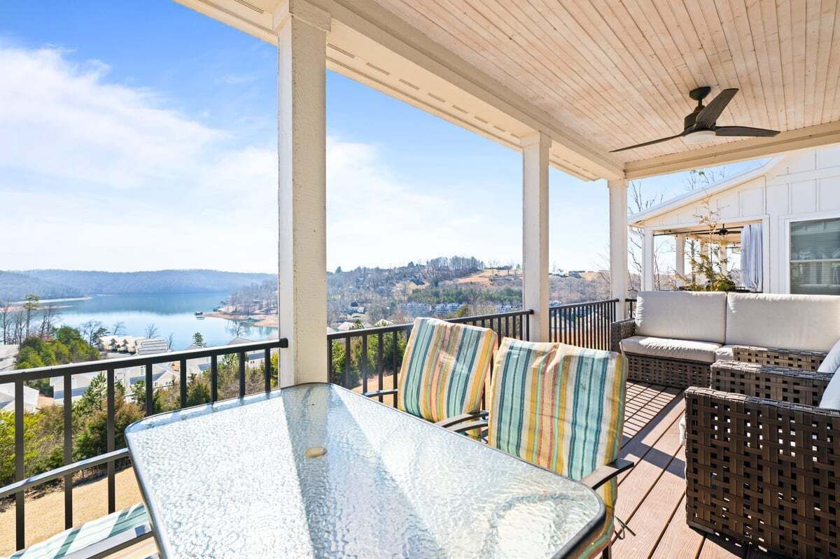 A covered outdoor seating area with a table and chairs, overlooking a lake and distant landscape.